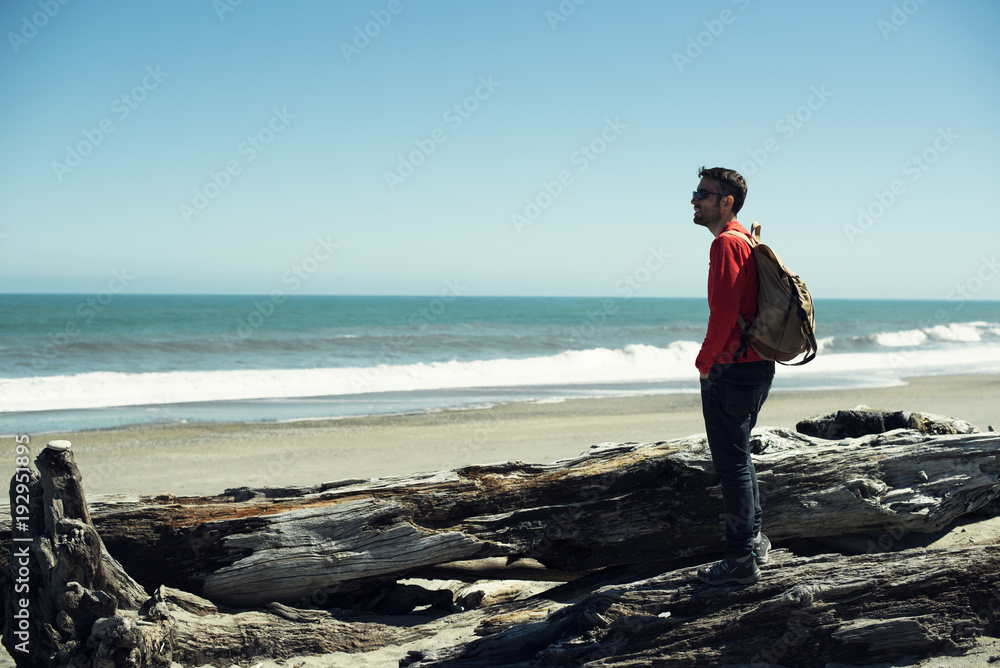 Retrato de hombre joven vestido de rojo frente a paisaje de playa minimalista con un amplio cielo azul.