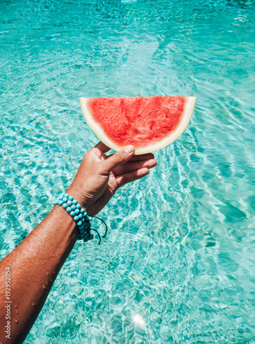 seedless watermelon in mens hand with pool on background