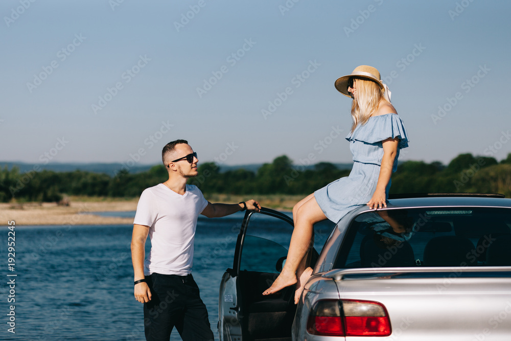 Happy traveler couple standing near car open trunk and watch the sunrise