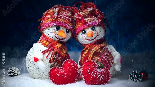 Valentine's Day. Snowmen in love stand on the snow and keep their hearts out of felt on a dark background