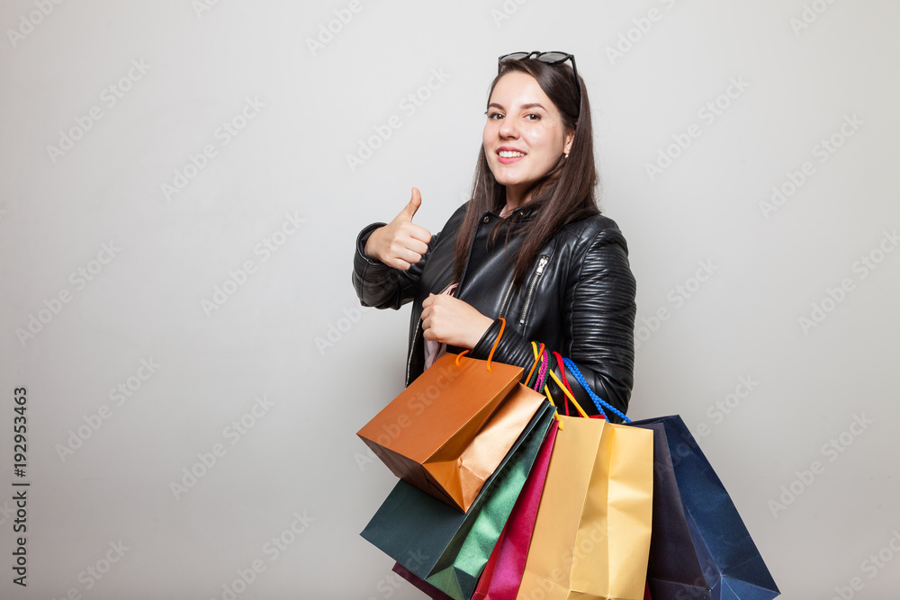 Attractive young woman shows thunb up during shopping trip standing in front of grey background Attractive young woman shows thunb up during shopping trip standing in front of grey background
