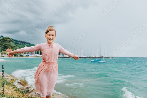 Sweet little girl playing by the lake on a very windy day wearing pink dress. Image taken on Lake Geneva, Lausanne, Switzerland