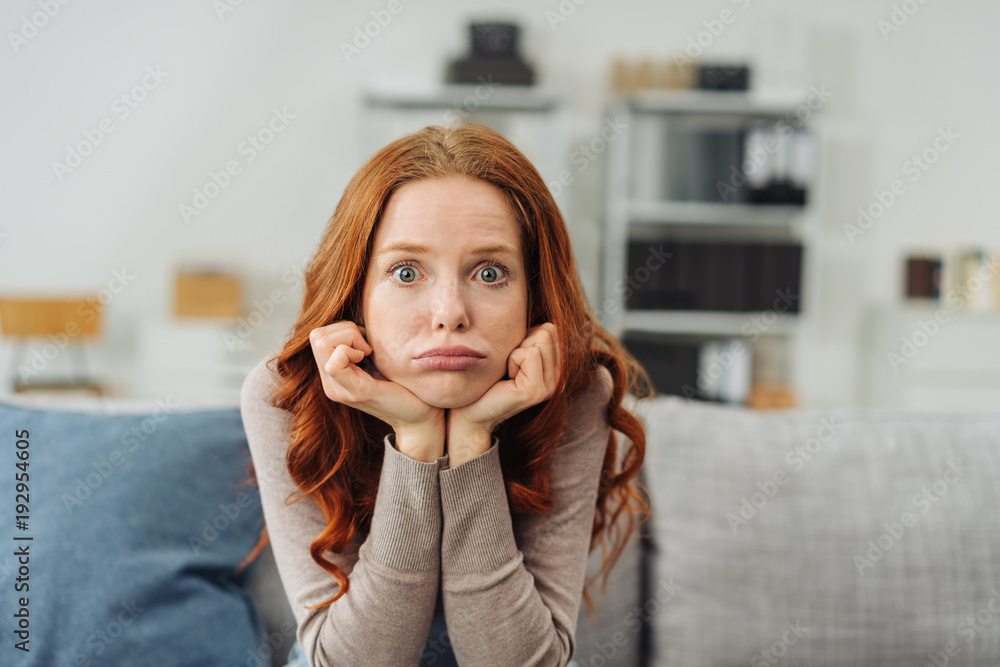 Young upset woman sitting on sofa at home - obrazy, fototapety, plakaty 