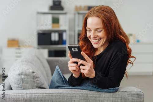 Young cheerful woman using mobile phone on sofa