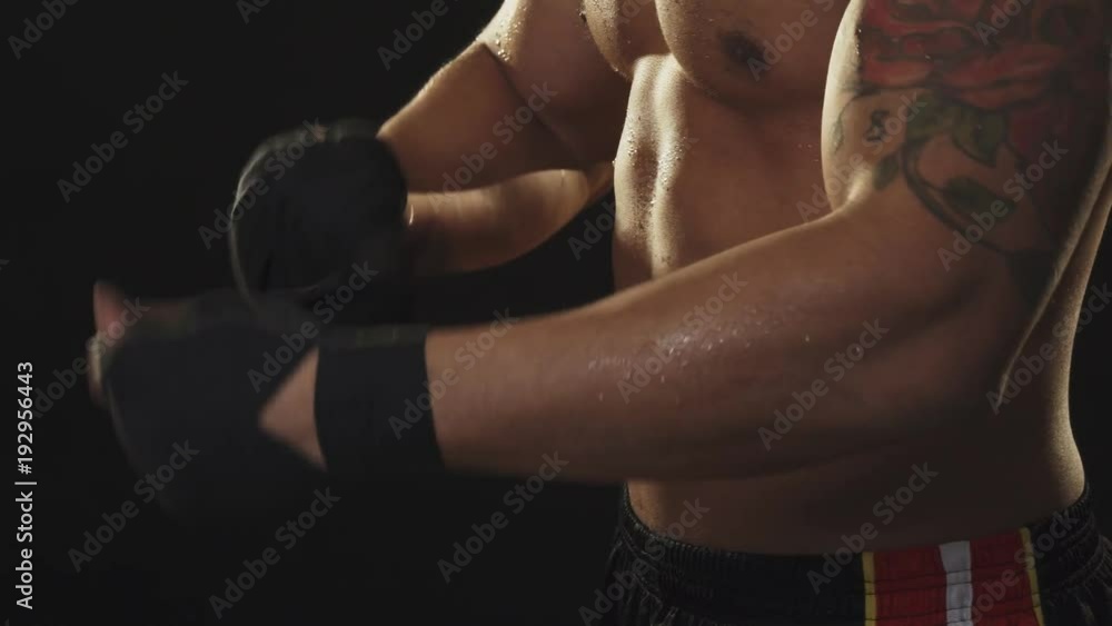 Ripped male boxer with sweaty torso taking off hand wraps after fighting Ripped male boxer with sweaty torso taking off hand wraps after fighting