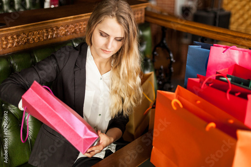 Curious young blond woman wants to know what is inside the shopping bags relaxing in a lobby