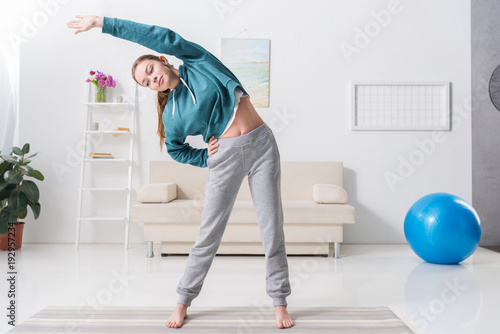 girl stretching body on yoga mat at home