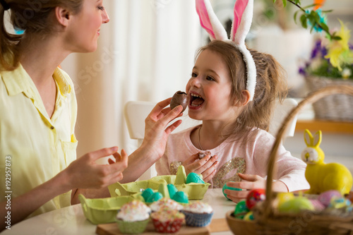 Mother and daughter celebrating Easter  eating chocolate eggs. Happy family holiday. Cute little girl in bunny ears laughing  smiling and having fun.