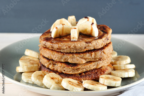 Buckwheat pancakes with bananas and chocolate syrup. A plate with pancakes is decorated with banana slices. Wooden background. Close-up. Macro photography.