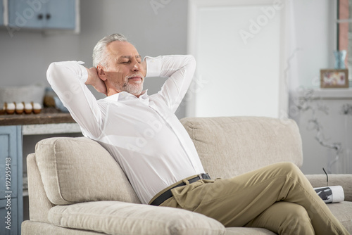 Time to dream. Positive delighted bearded man crossing legs while sitting on the sofa, stretching arms © zinkevych
