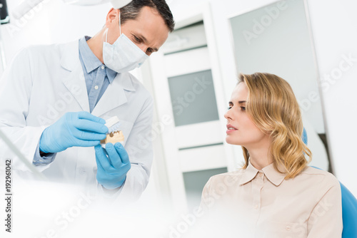 Doctor showing jaws model to female patient in modern dental clinic
