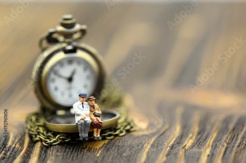 Miniature people : Couple of love sitting with vintage pocket watch on wood background,vintage retro concept.