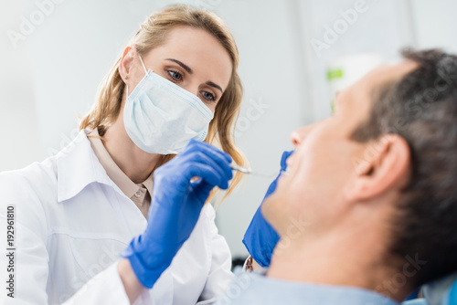 Doctor checking patient teeth with mirror in modern dental clinic