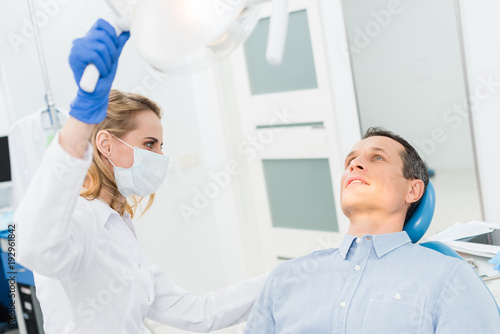 Female dentist adjusting lamp in modern dental clinic