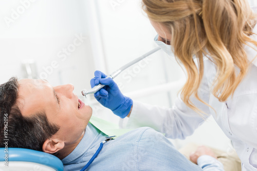 Male patient at dental procedure using dental drill in modern dental clinic
