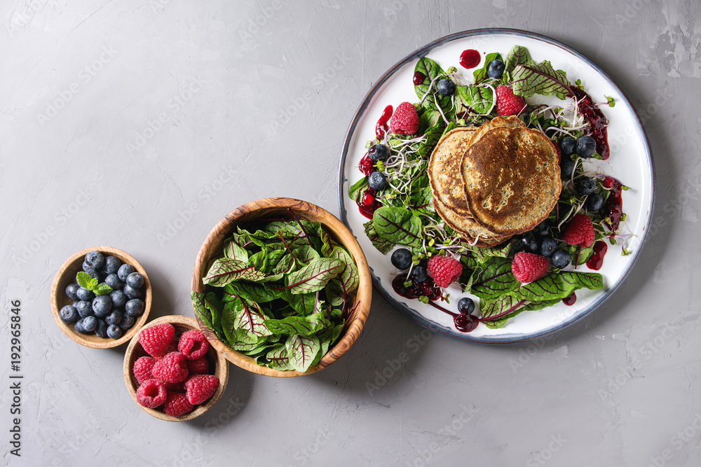 Vegan chickpea pancakes served in plate with green salad young beetroot leaves, sprouts, berries, berry sauce. Ingredients in bowls above over grey concrete background. Top view, space. Healthy eating Vegan chickpea pancakes served in plate with green salad young beetroot leaves, sprouts, berries, berry sauce. Ingredients in bowls above over grey concrete background. Top view, space. Healthy eating