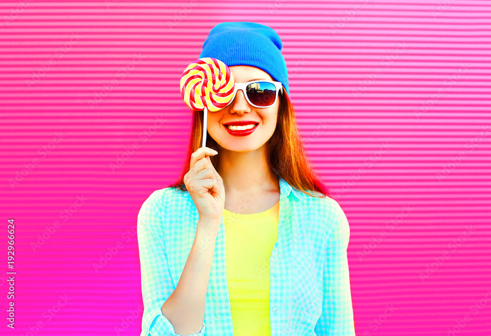 portrait happy smiling woman hides her eye with a lollipop on stick on pink colorful background