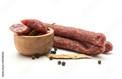 Three Hungarian dry sausages pepperoni with black pepper and bay leaves cut pieces in a wooden bowl isolated on white background smoked in natural casing mixed pork and beef.