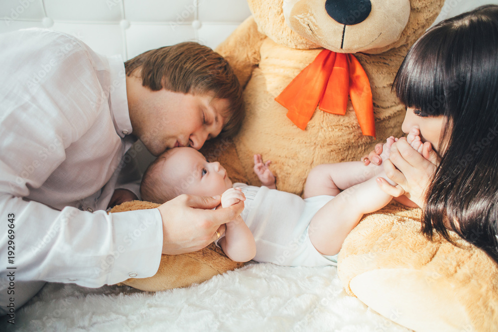 The mother,father and son lie near bear on the bed