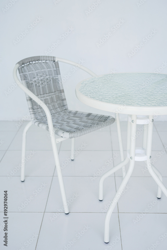 Transparent white table in the cafe. Rattan chair in the background. The whole room is white. Side view with copy space Transparent white table in the cafe. Rattan chair in the background. The whole room is white. Side view with copy space