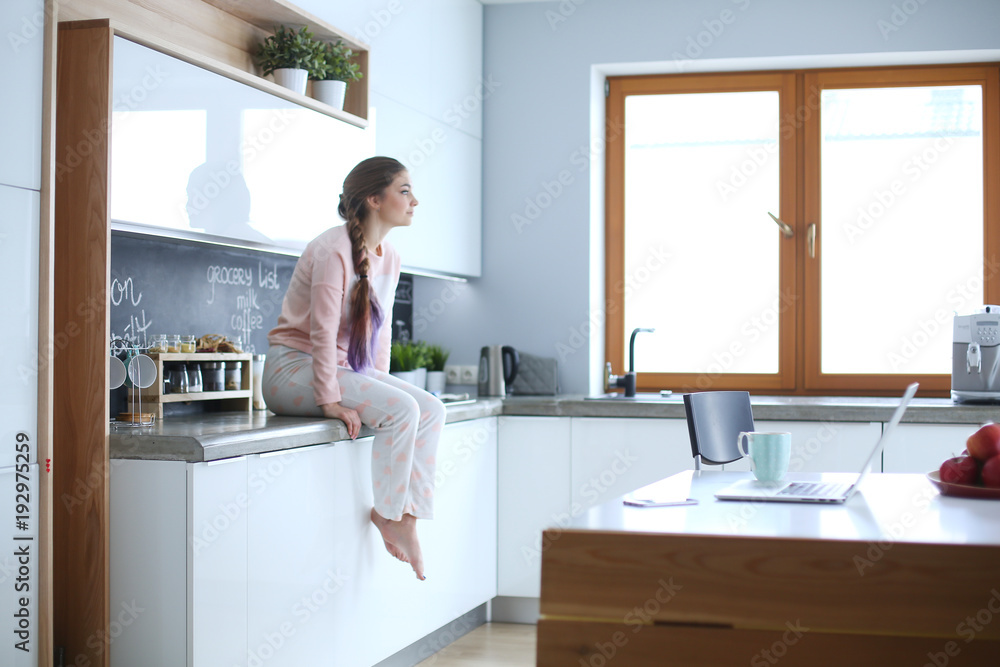 Young woman sitting on table in the kitchen. Young woman sitting on table in the kitchen.