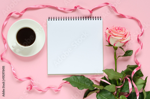 Pink blooming fresh rose flower with cup for coffee and notebook on pink background © Moseva_Alena
