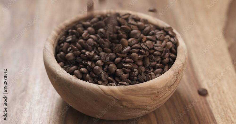 Fototapeta premium coffee beans falling into wood bowl on table
