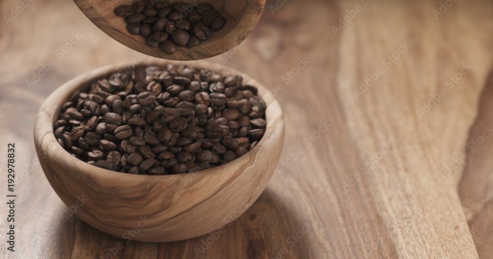 coffee beans falling into wood bowl on table coffee beans falling into wood bowl on table