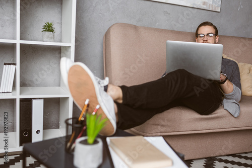 stylish young freelancer working with laptop on couch