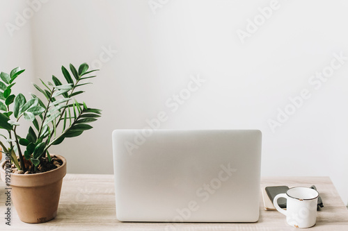 Laptop on wooden desktop with phone, notebook, coffee cup and plant in stylish modern room. Freelance concept. business workspace in home or office. stylish work place. working online