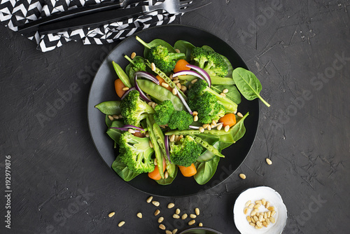 Vegetarian dinner snack salad of broccoli, young peas, baby carrots, sweet onions with pine nuts. Top View. photo