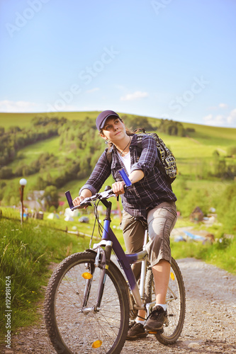 Young woman is traveling with a bicycle in the summer mountains