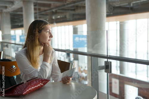 Young beautiful girl sits at table with ticket and waits for airplane photo