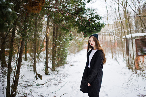 Fashionable long legs brunette model in long black cloak and hat outdoor at winter day.