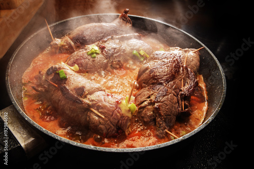 cooking beef roulades, german stuffed meat rolls with vegetables and sauce steaming in a pan on the black stove