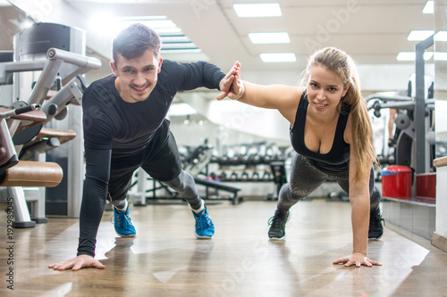 Happy sporty couple giving high five to each other while doing push ups together in the gym.