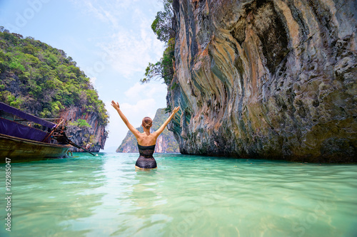 Vacation and freedom. Happy young woman rising hands up standing on tropical beach enjoying beautiful view in Thailand.