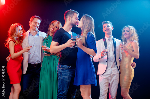 Party and celebration. Couple kissing. Group of seven happy smiling friends having fun together in night club.