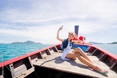 Happy vacation in Thailand. Pretty young woman taking selfie on smartphone sailing the sea on traditional longtail boat. © luengo_ua