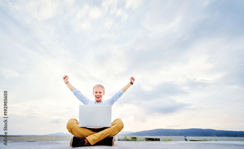 Winner businessman. Young excited man working on laptop while sitting on the roof top.