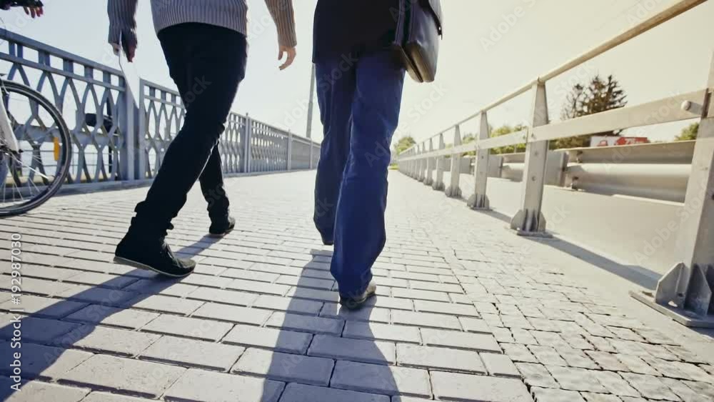 Two businessmen walking over a bridge in a low angle view of their legs with a cyclist on a bicycle passing them on the left and disappearing into the distance. Two businessmen walking over a bridge in a low angle view of their legs with a cyclist on a bicycle passing them on the left and disappearing into the distance.