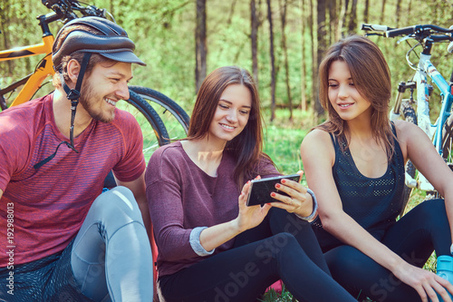 Group of young friends hiking through the forest with bikes on a © Fxquadro