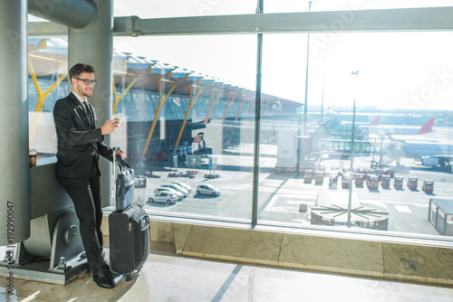 handsome businessman standing waiting for his flight at the airport close to the terminal window