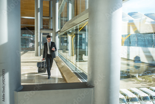 young businessman walking at the airport using his mobile phone