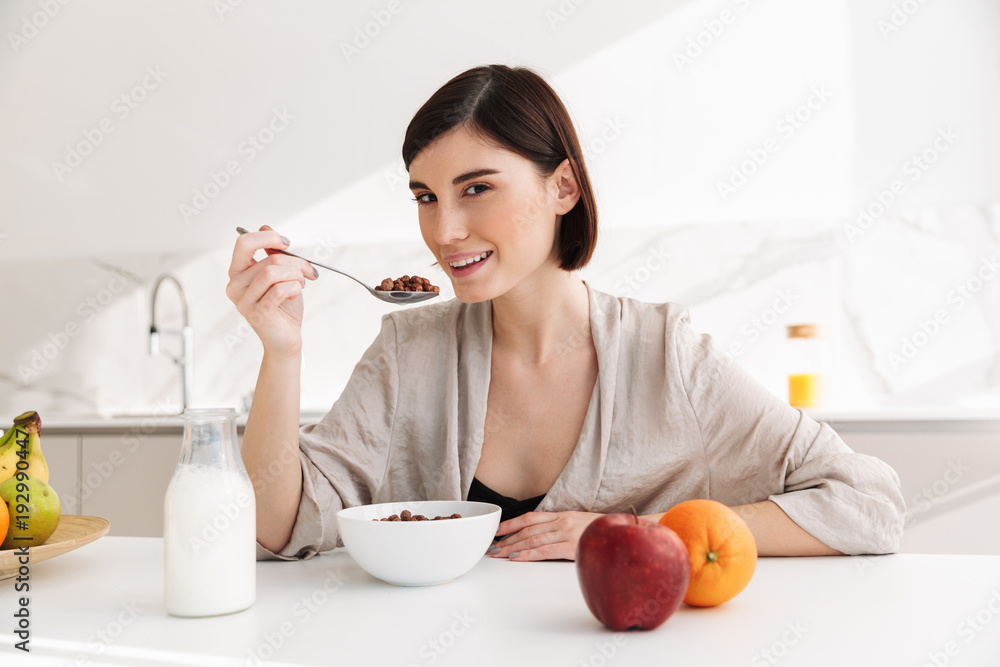 Photo of healthy young woman having breakfast in kitchen at home, and eating cocoa balls with milk Photo of healthy young woman having breakfast in kitchen at home, and eating cocoa balls with milk