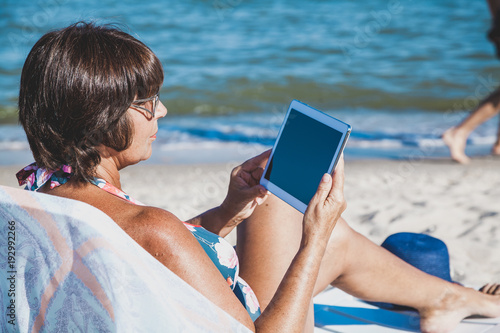 Elderly woman with tablet on beach