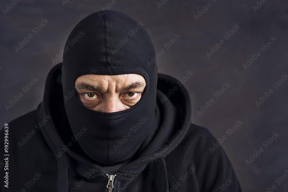 A man in a balaclava on a dark background. Copy space. Concept stealing, deception