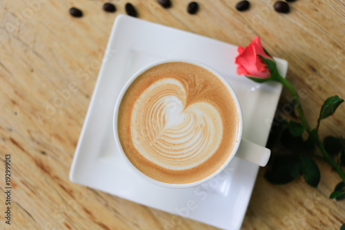 Top view Coffee latte art heart shape with a pink rose and coffee beans on wood table.