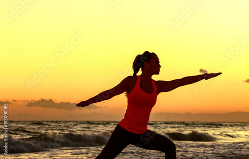 Silhouette of fit woman in sport clothes on beach stretching