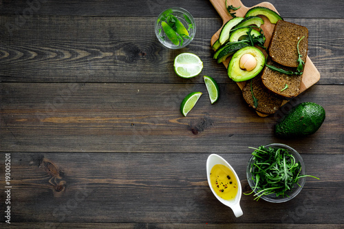 Breakfast for safety weight loss. Avocado toast with rye bread, lime, olive oil and greens on dark wooden background top view space for text